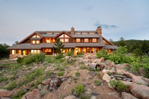 Luxury real estate home on 11780 Gold Hill, set on 108 acres in Boulder County, showcasing a rustic mountain design with large windows, stone accents, and surrounded by rugged natural terrain.