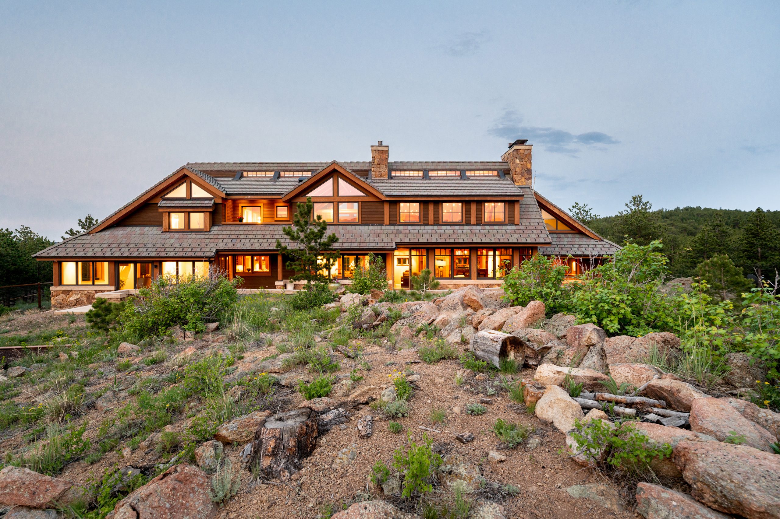 Luxury real estate home on 11780 Gold Hill, set on 108 acres in Boulder County, showcasing a rustic mountain design with large windows, stone accents, and surrounded by rugged natural terrain.