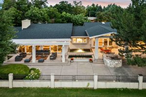 Outdoor living space of a luxury real estate home featuring a spacious covered patio with modern outdoor seating, a peaceful water feature, and a built-in stone grill, surrounded by lush greenery, perfect for entertaining or relaxing in style.