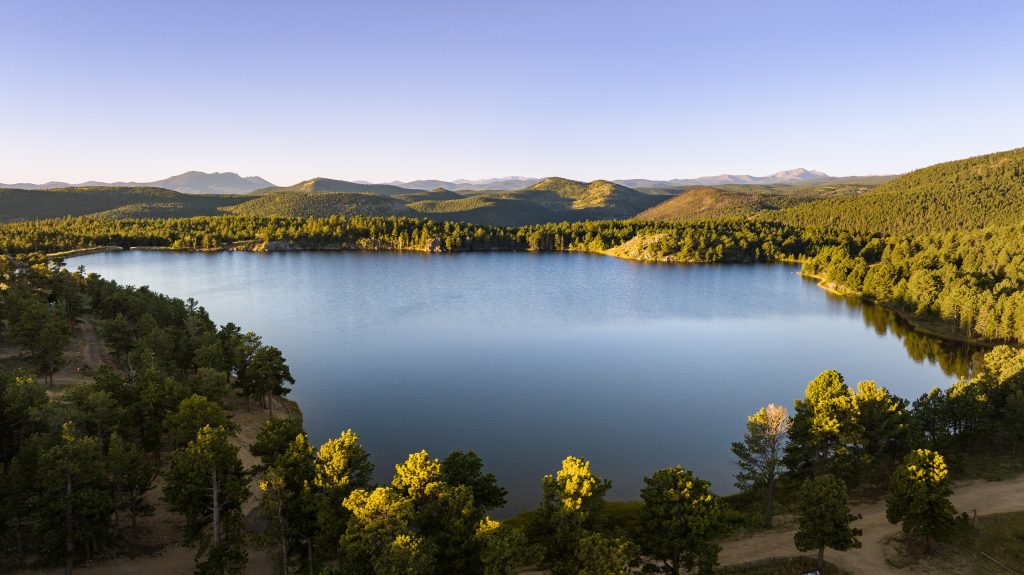 A breathtaking aerial view of Gold Lake, a 99-acre historic luxury real estate property in Boulder County, surrounded by forested hills and expansive mountain views.