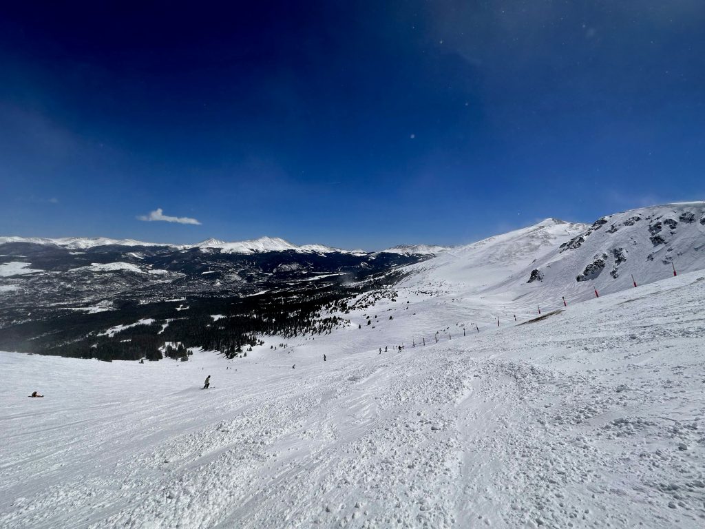 A snowy mountain landscape with skiers on a slope under a clear blue sky.