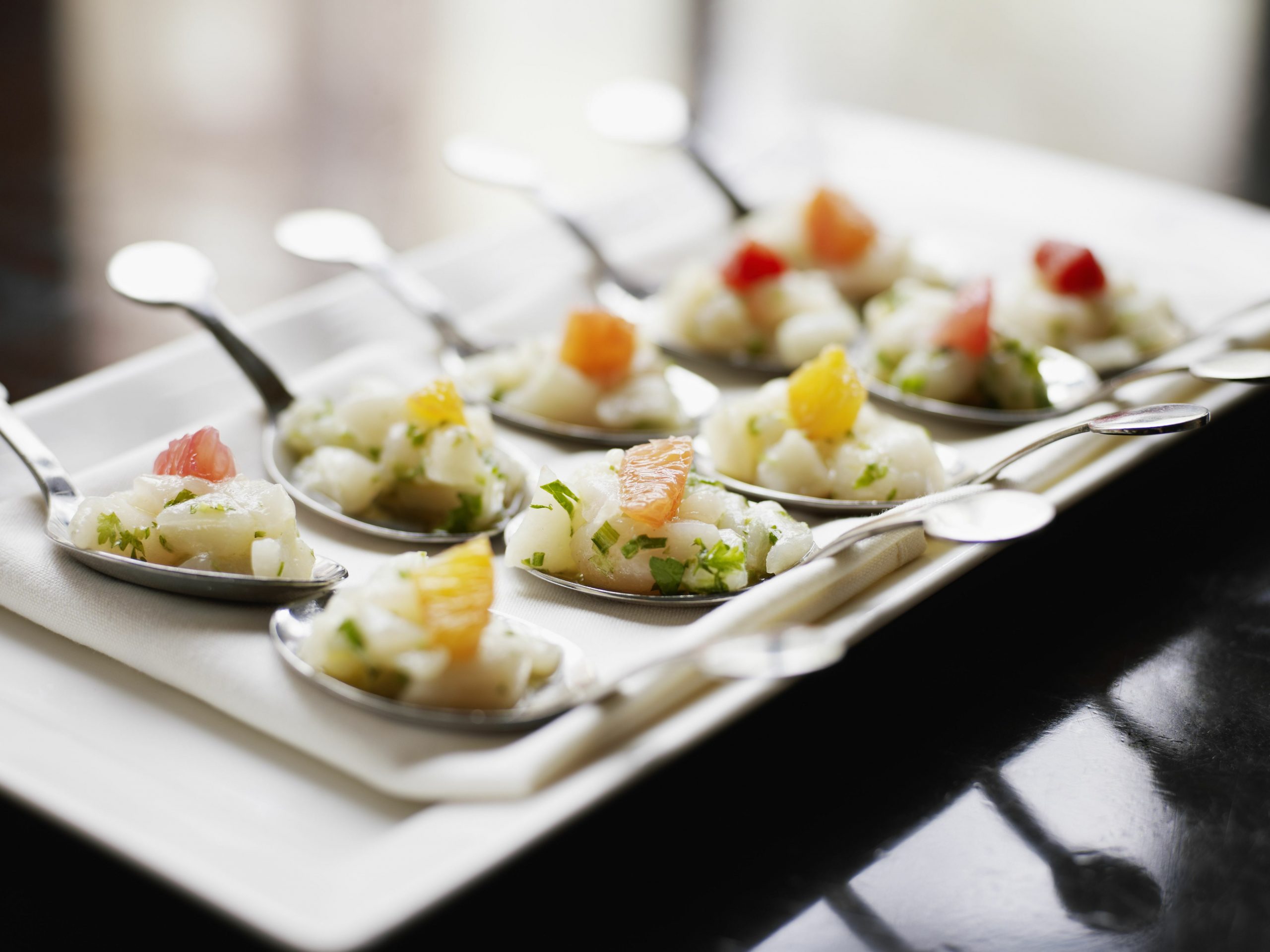 Appetizer spoons of ceviche with herbs and citrus on a white plate.