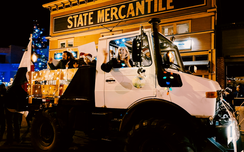 Festive holiday parade with a decorated truck in front of State Mercantile.