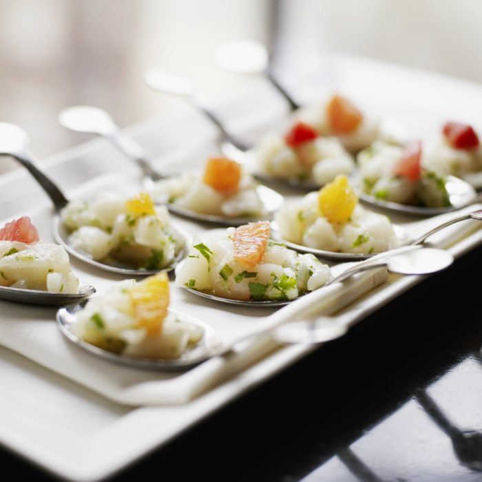 Appetizer spoons of ceviche with herbs and citrus on a white plate.